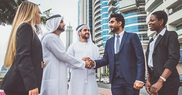 Business delegates in suits and kanduras shaking hands in Dubai’s business district