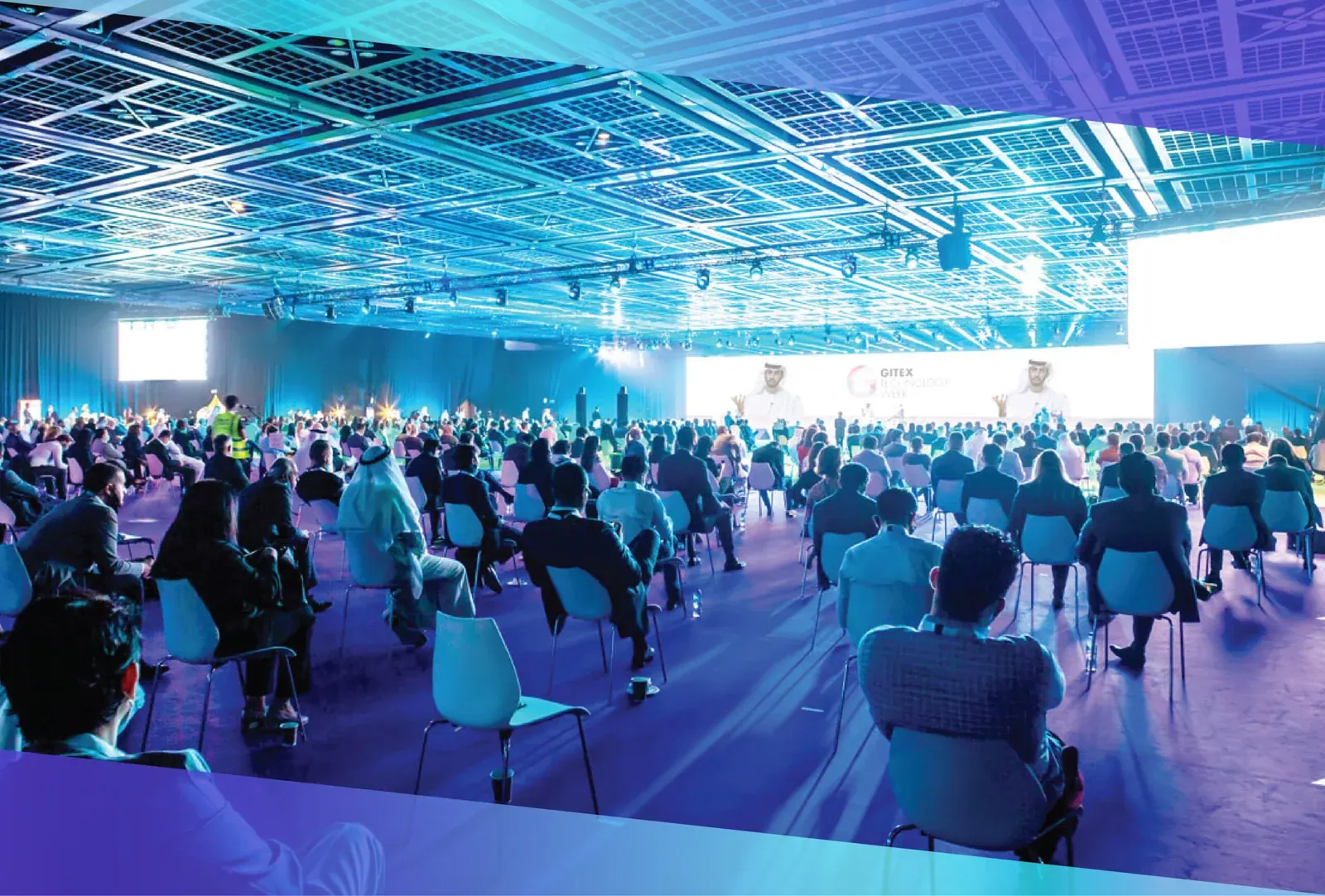 A packed conference auditorium under blue stage lighting
