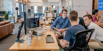 Founders in conversation across a desk in an open-plan technology office